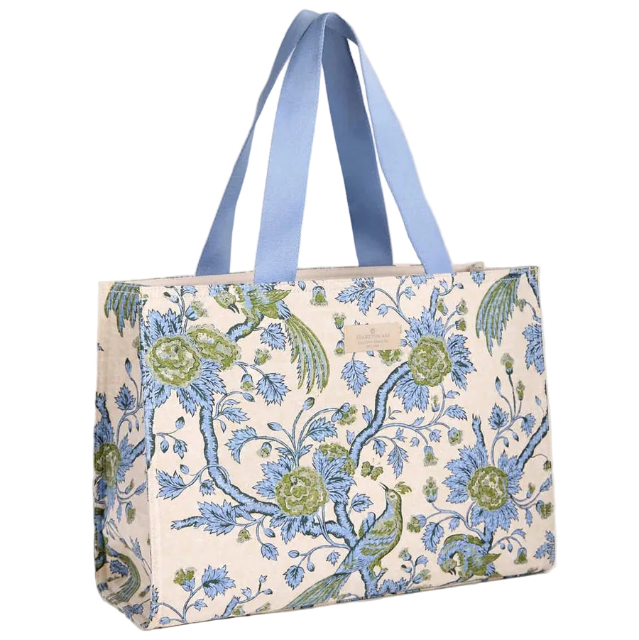 A tote bag featuring a blue and green floral tapestry pattern on a cream background, with light blue fabric shoulder straps, shown against a solid light beige background.