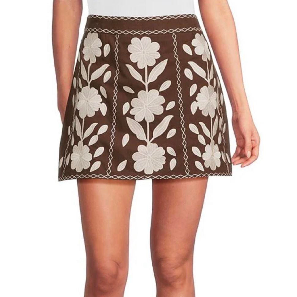 A brown mini skirt with cream floral embroidery, shown on a model from the waist down against a white background.